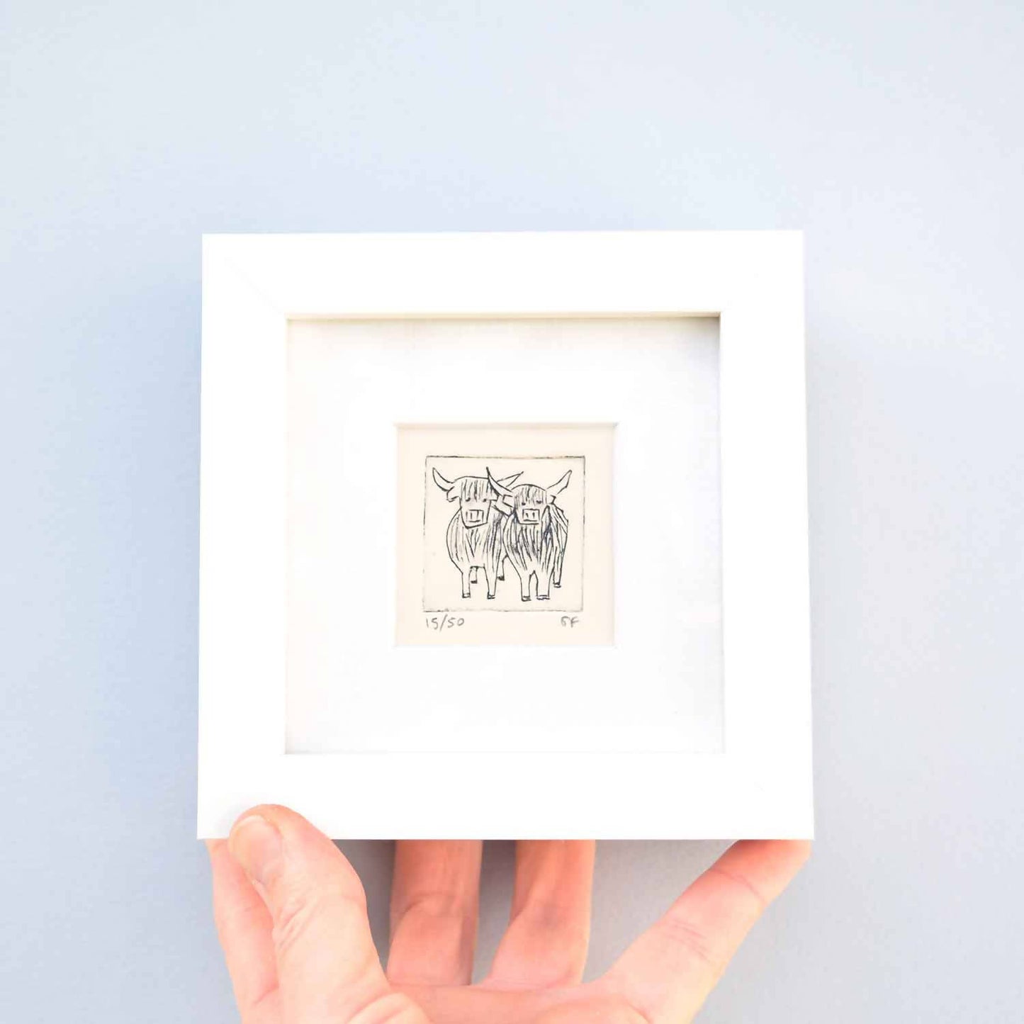 Two highland cows standing close - mini collagraph print in a white frame